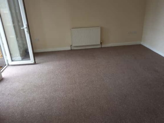 This is a photo of a living room after it has been cleaned. The room is empty and has a brown carpet that has been steam cleaned works carried out by Hendon Carpet Cleaning